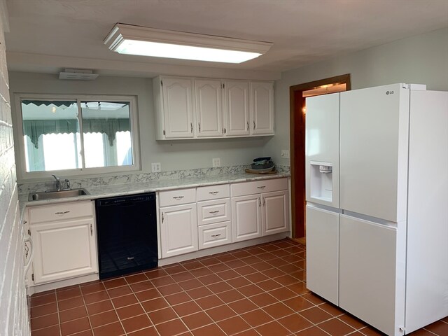 kitchen with sink, white refrigerator with ice dispenser, dark tile patterned flooring, black dishwasher, and white cabinetry