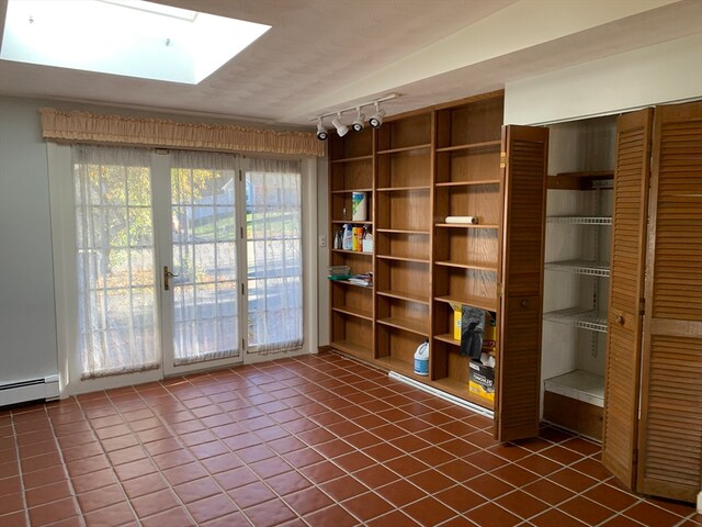 unfurnished room with track lighting, a baseboard heating unit, dark tile patterned floors, and a skylight