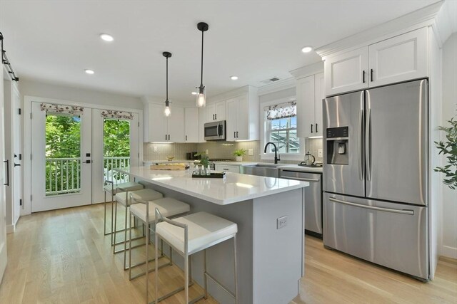 176 Medford St Unit 176, Arlington, MA 02474 - kitchen featuring appliances with stainless steel finishes, a center island, white cabinetry, decorative backsplash, and light countertops