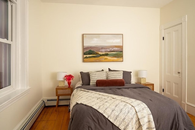 bedroom featuring a baseboard heating unit, baseboards, and wood finished floors