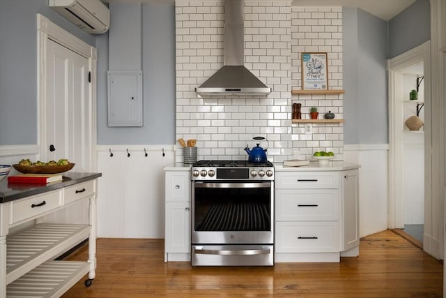 kitchen featuring wall chimney range hood, gas range, electric panel, wainscoting, and a wall mounted AC