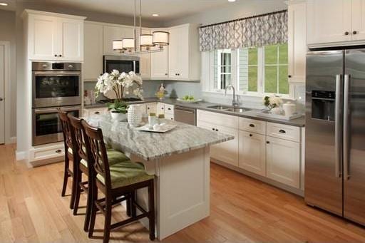 kitchen with pendant lighting, a kitchen island, stainless steel appliances, light hardwood / wood-style floors, and white cabinets