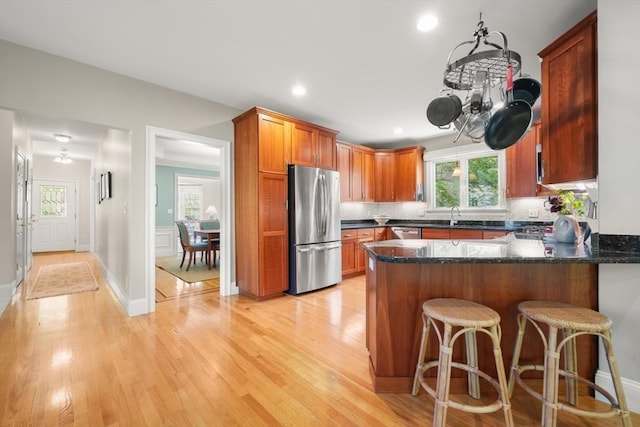 kitchen featuring a peninsula, dark stone countertops, light wood-type flooring, appliances with stainless steel finishes, and tasteful backsplash