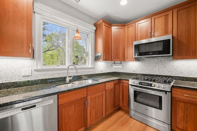 kitchen featuring a sink, brown cabinetry, dark stone countertops, and appliances with stainless steel finishes