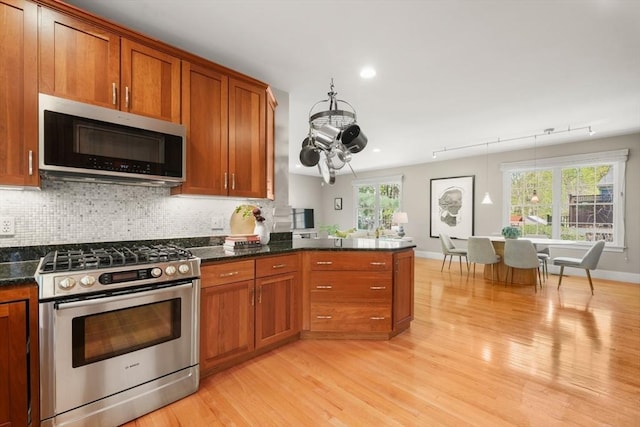 kitchen featuring brown cabinetry, stainless steel appliances, decorative backsplash, and light wood-style floors