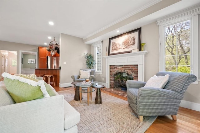 living room with ornamental molding, light wood-type flooring, recessed lighting, a brick fireplace, and baseboards