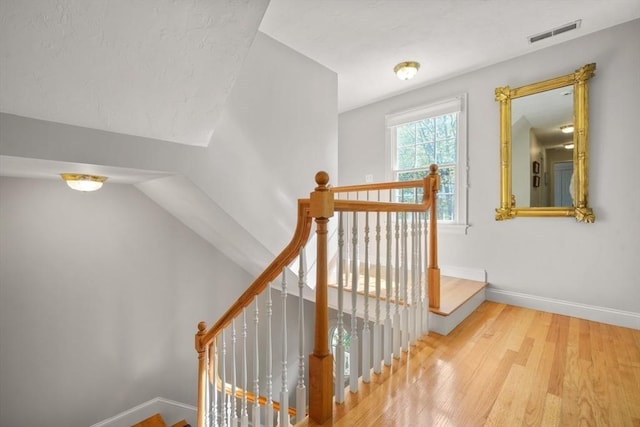 staircase with vaulted ceiling, visible vents, wood finished floors, and baseboards