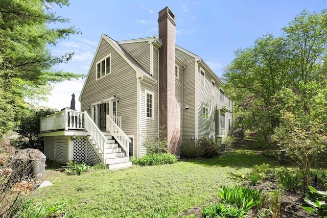 rear view of house featuring a chimney, stairs, a wooden deck, and a lawn