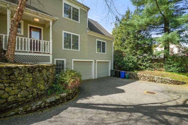 view of side of property with an attached garage, a porch, and driveway