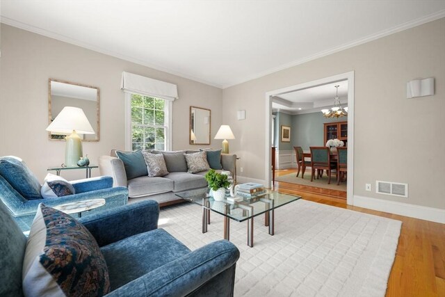 living area with wood finished floors, a notable chandelier, visible vents, baseboards, and ornamental molding