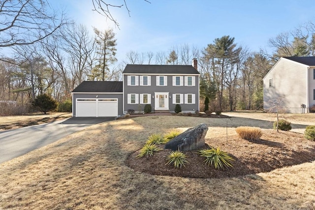 colonial home featuring an attached garage, driveway, and a chimney