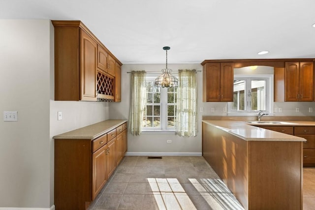 kitchen featuring brown cabinetry, a peninsula, light countertops, and baseboards