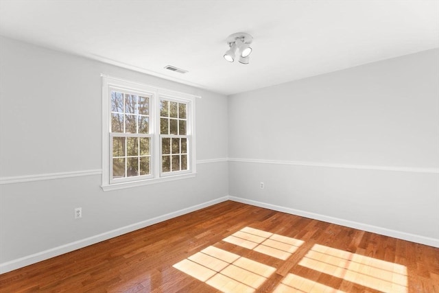 empty room featuring visible vents, baseboards, and wood finished floors