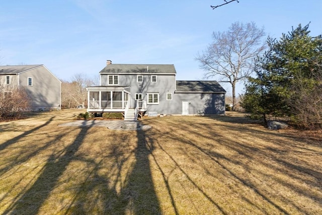 rear view of property with a lawn, a chimney, and a sunroom