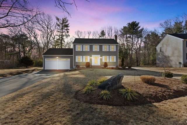 colonial-style house featuring a garage, concrete driveway, and a chimney