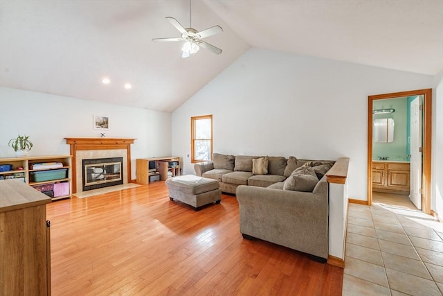 living room with a tiled fireplace, light hardwood / wood-style flooring, high vaulted ceiling, and ceiling fan