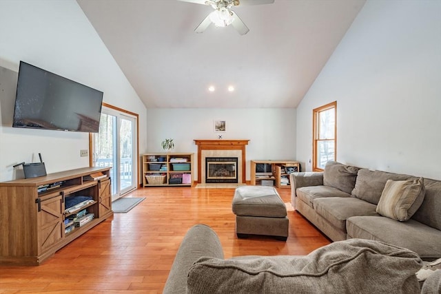 living room with a tiled fireplace, high vaulted ceiling, light hardwood / wood-style floors, and ceiling fan