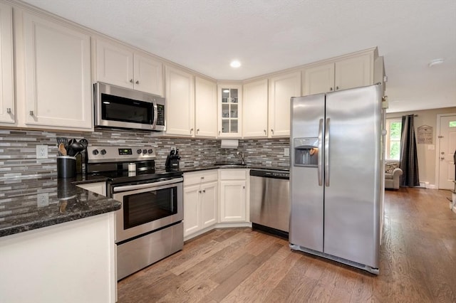 1608 Plymouth St Unit 1608, East Bridgewater, MA 02333 - kitchen featuring appliances with stainless steel finishes, light wood finished floors, decorative backsplash, dark stone countertops, and glass insert cabinets
