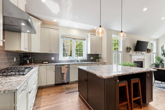 109 Phoebe St Unit 109, Methuen, MA 01844 - kitchen featuring appliances with stainless steel finishes, wall chimney range hood, a center island, light wood finished floors, and decorative backsplash