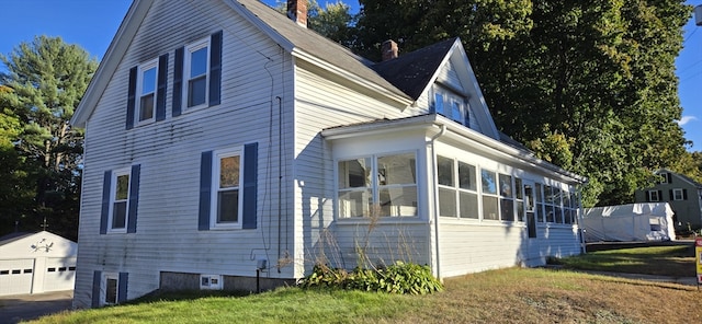 view of property exterior with a yard, an outbuilding, a sunroom, and a garage