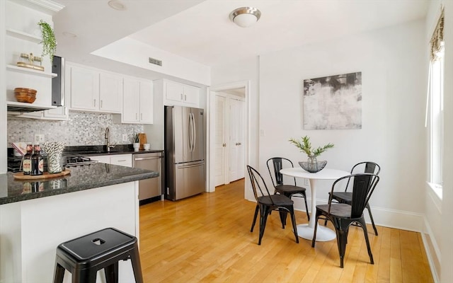 kitchen with appliances with stainless steel finishes, open shelves, white cabinets, backsplash, and light wood-type flooring
