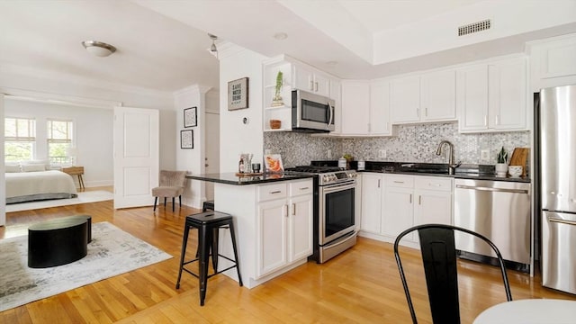kitchen with stainless steel appliances, a sink, backsplash, white cabinetry, and light wood finished floors