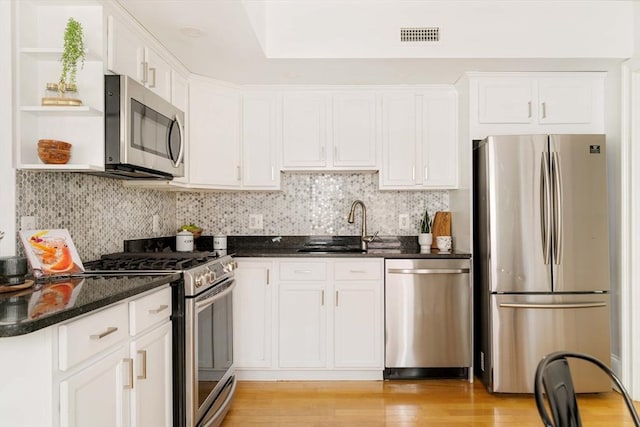 kitchen featuring appliances with stainless steel finishes, open shelves, white cabinets, dark stone counters, and a sink