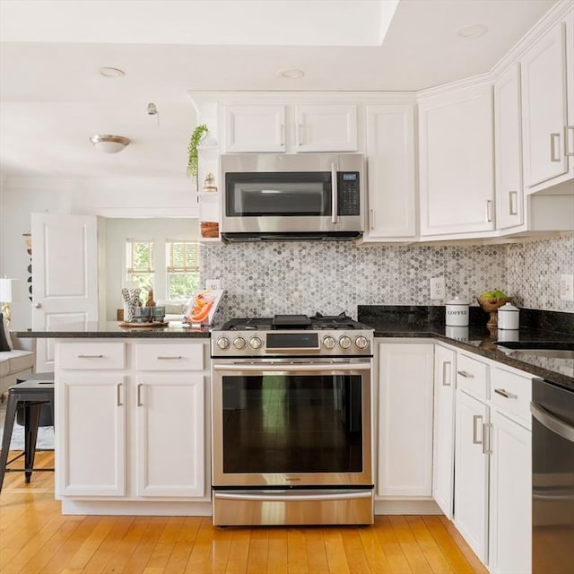 kitchen with appliances with stainless steel finishes, white cabinets, light wood-style flooring, tasteful backsplash, and dark stone countertops