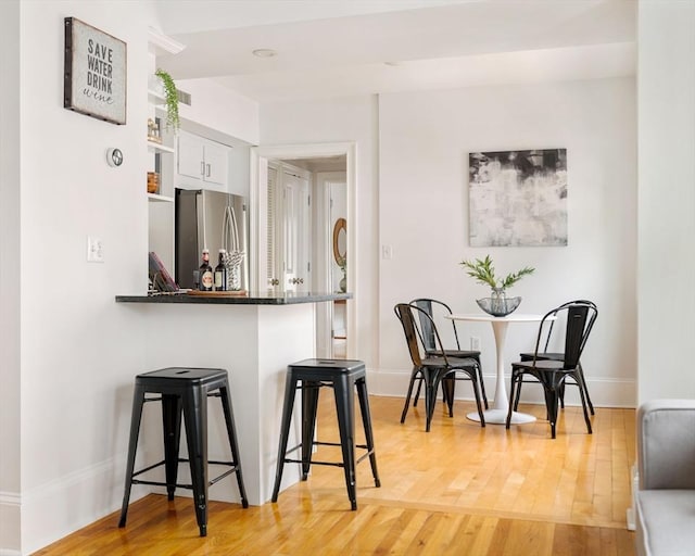kitchen featuring freestanding refrigerator, a breakfast bar area, white cabinets, light wood-type flooring, and open shelves