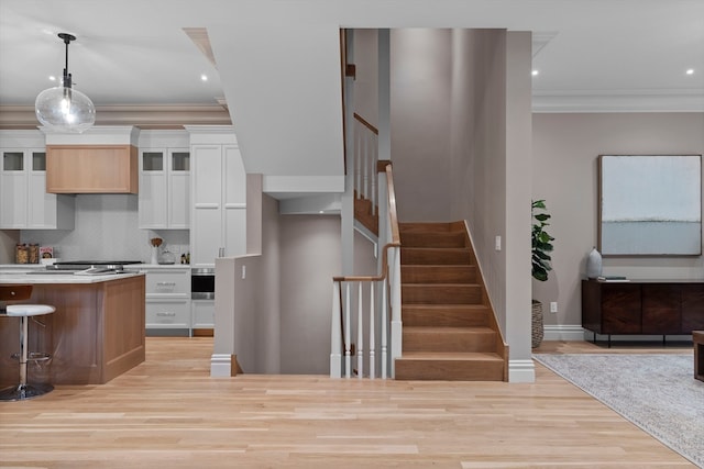 interior space featuring light wood-type flooring, white cabinetry, a breakfast bar area, pendant lighting, and ornamental molding