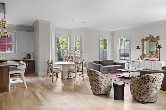 living area with light wood-style flooring, plenty of natural light, baseboards, and ornamental molding