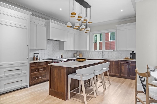 kitchen with a sink, tasteful backsplash, a center island, a breakfast bar area, and light wood finished floors