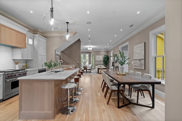 kitchen with a kitchen island with sink, premium range, white cabinetry, decorative light fixtures, and light hardwood / wood-style floors