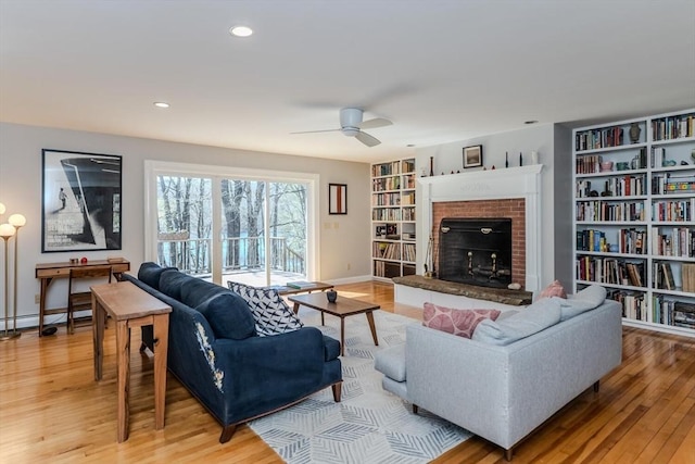 living room featuring light wood-style floors, a brick fireplace, baseboard heating, and ceiling fan