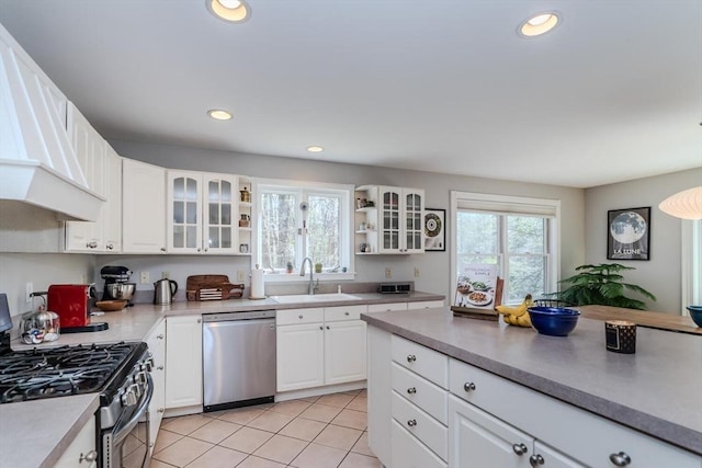 kitchen with a sink, stainless steel appliances, white cabinetry, light tile patterned floors, and glass insert cabinets