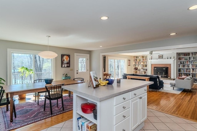kitchen featuring a center island, a fireplace, light tile patterned floors, light countertops, and white cabinets