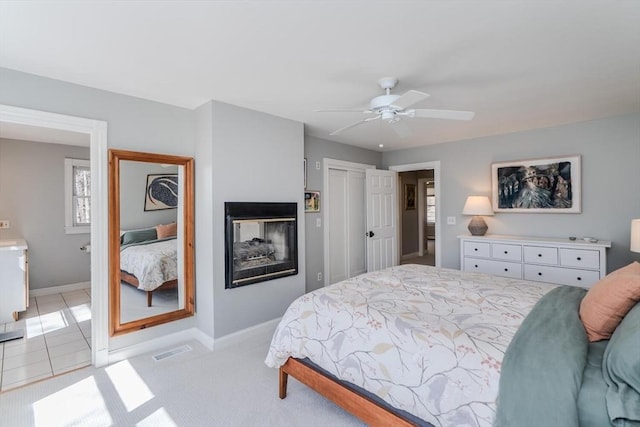 bedroom with visible vents, a closet, baseboards, ceiling fan, and a multi sided fireplace
