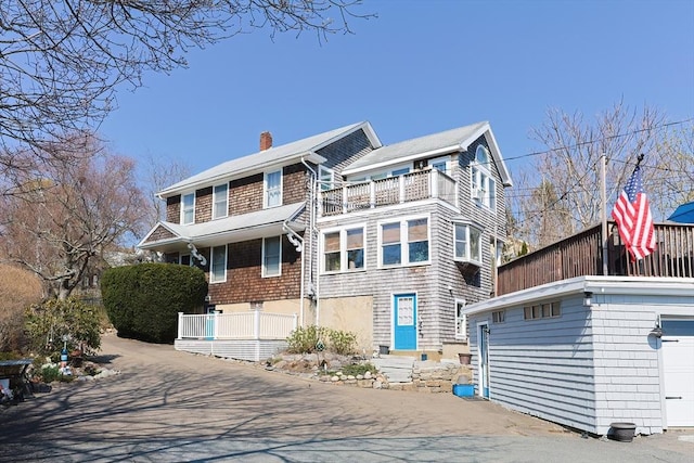 view of front of home featuring a porch, a chimney, and a balcony