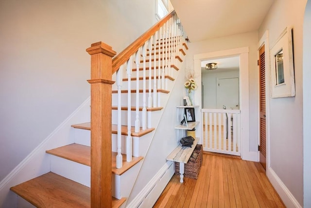 staircase with wood-type flooring, a baseboard heating unit, and baseboards