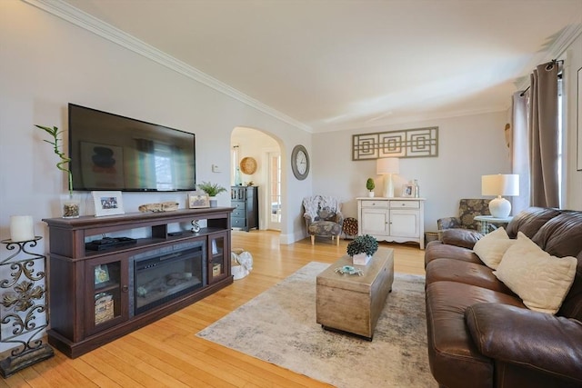 living area with crown molding, arched walkways, and light wood-style floors