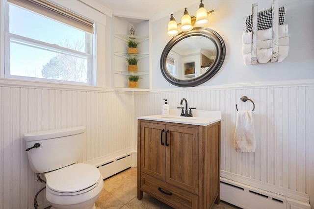 half bath with vanity, toilet, a wainscoted wall, and a baseboard heating unit