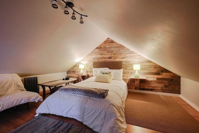 bedroom with rail lighting, wood finished floors, wooden walls, and vaulted ceiling