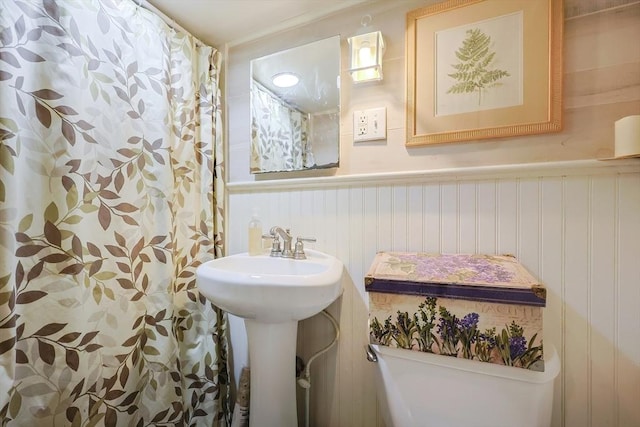 bathroom featuring a shower with curtain, a wainscoted wall, a sink, and toilet