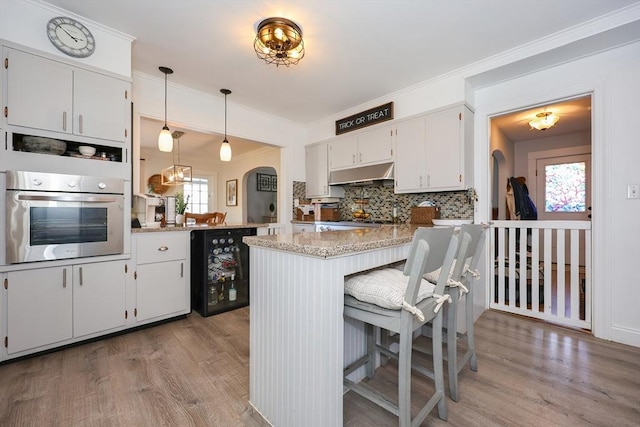 kitchen featuring light wood-style floors, a peninsula, under cabinet range hood, and oven