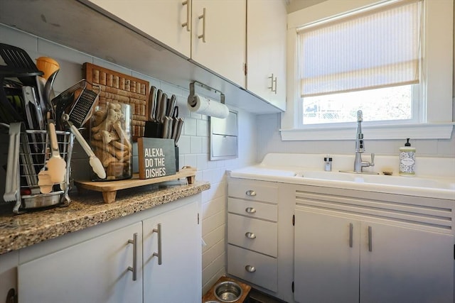 interior space featuring white cabinetry, backsplash, light countertops, and a sink
