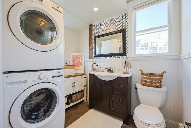 bathroom with stacked washing maching and dryer, vanity, toilet, and a wainscoted wall