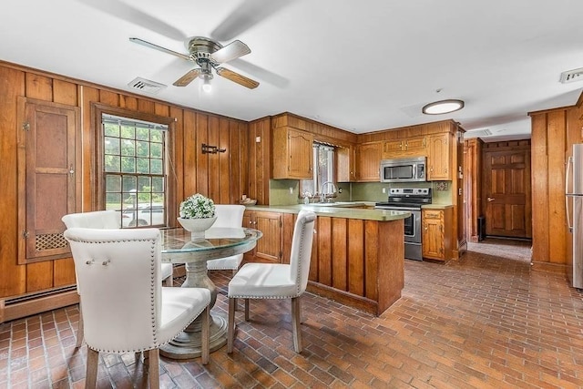 57 Rudon Dr, North Attleboro, MA 02760 - kitchen featuring appliances with stainless steel finishes, brick flooring, wood walls, a peninsula, and brown cabinetry