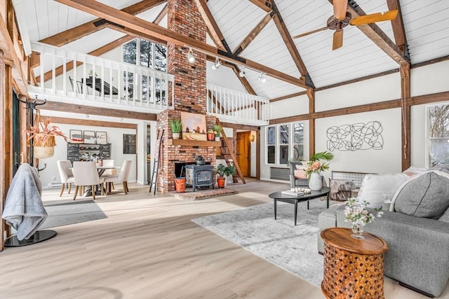 living room with beamed ceiling, ceiling fan, a wood stove, and light hardwood / wood-style floors