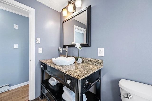 bathroom with baseboards, toilet, baseboard heating, wood finished floors, and vanity