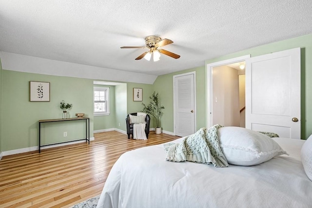 bedroom with light wood-type flooring, a ceiling fan, a textured ceiling, baseboards, and vaulted ceiling